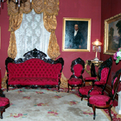 Antique parlor restored — crimson tufted seating, gilded carved frames, period portrait wall